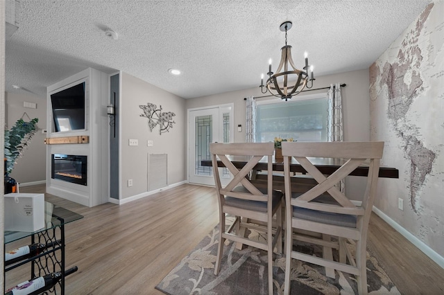 dining room with a textured ceiling, a notable chandelier, a large fireplace, wood finished floors, and visible vents