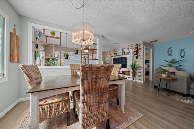 dining room featuring light wood-type flooring, visible vents, a notable chandelier, and a textured ceiling