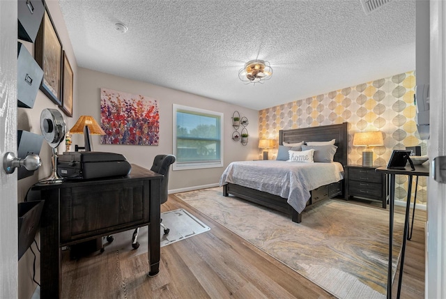 bedroom with wallpapered walls, baseboards, an accent wall, wood finished floors, and a textured ceiling