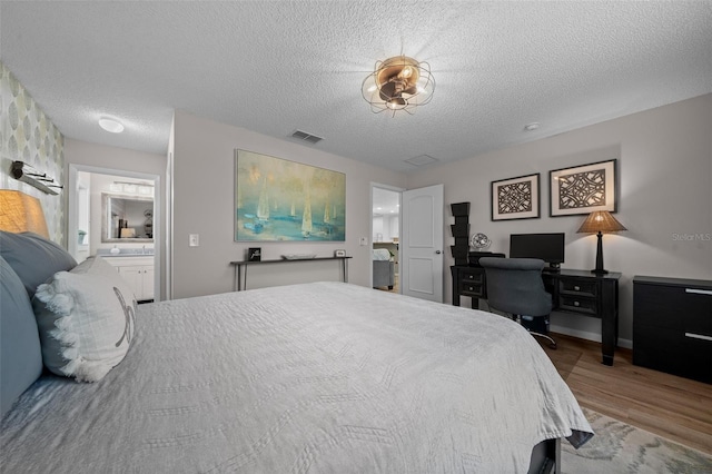 bedroom with visible vents, a textured ceiling, ensuite bathroom, and wood finished floors