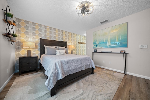 bedroom with an accent wall, wood finished floors, visible vents, and baseboards