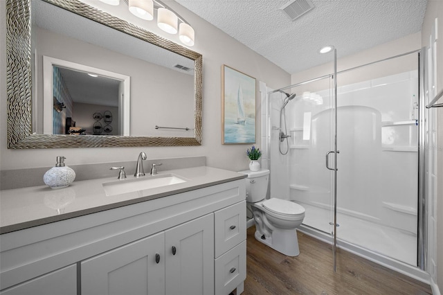 bathroom with a textured ceiling, wood finished floors, a shower stall, and visible vents