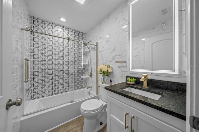 bathroom featuring toilet, bath / shower combo with glass door, wood finished floors, vanity, and tile walls