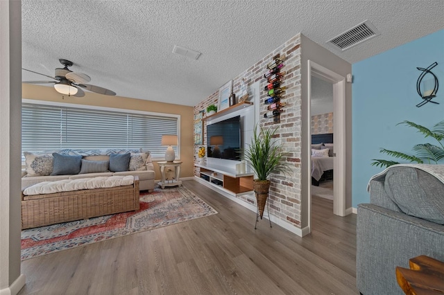 living area featuring a ceiling fan, visible vents, baseboards, and wood finished floors