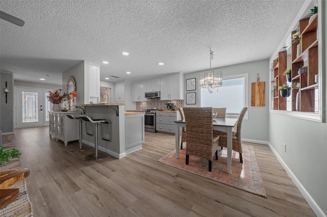 dining area with light wood finished floors, baseboards, a textured ceiling, a notable chandelier, and recessed lighting