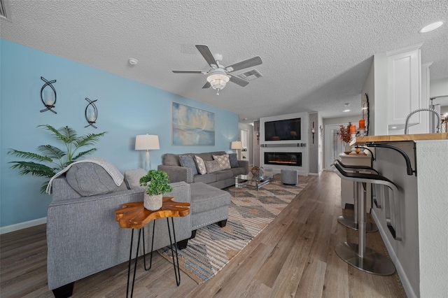 living room featuring ceiling fan, wood finished floors, visible vents, baseboards, and a glass covered fireplace