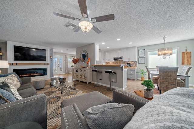 living area with light wood finished floors, recessed lighting, visible vents, a glass covered fireplace, and ceiling fan with notable chandelier