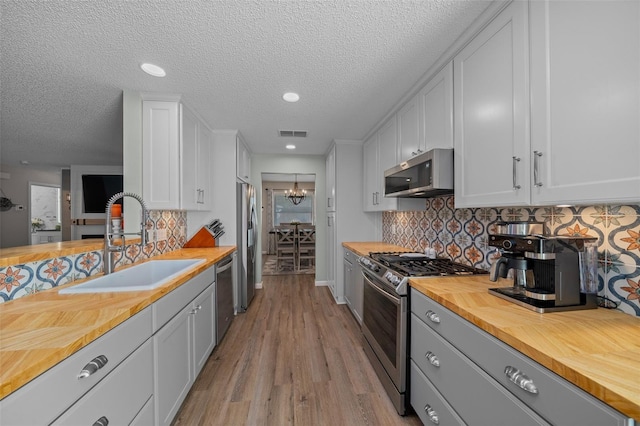 kitchen featuring visible vents, white cabinets, butcher block counters, stainless steel appliances, and a sink