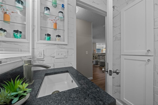 bathroom with tile walls, tasteful backsplash, a sink, a textured ceiling, and wood finished floors