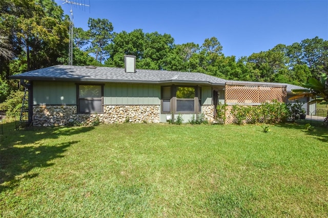 back of property with a shingled roof, stone siding, a lawn, and a chimney