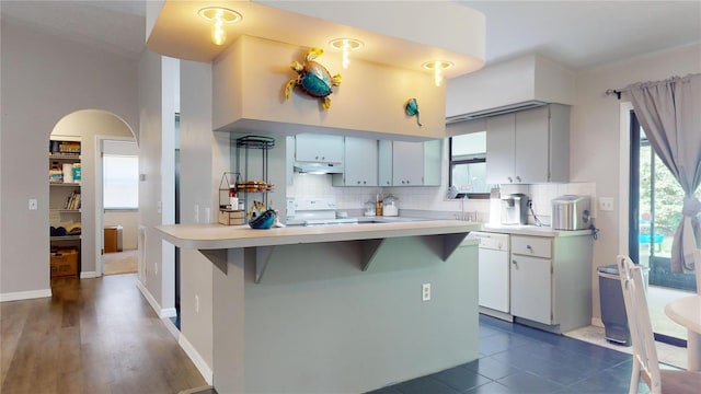 kitchen with light countertops, decorative backsplash, a healthy amount of sunlight, white appliances, and under cabinet range hood