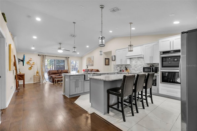 kitchen with lofted ceiling, visible vents, open floor plan, a kitchen island, and a peninsula