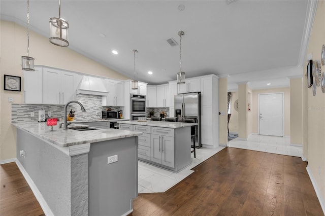 kitchen featuring visible vents, lofted ceiling, appliances with stainless steel finishes, light stone counters, and a sink
