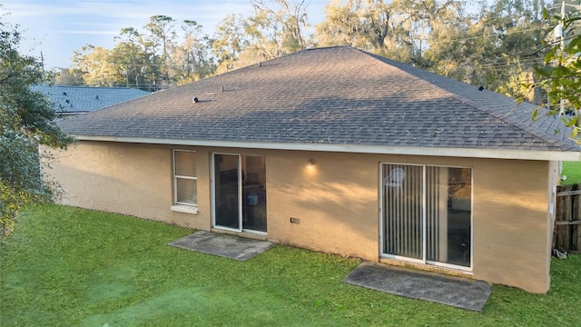 back of property with roof with shingles, a lawn, and stucco siding