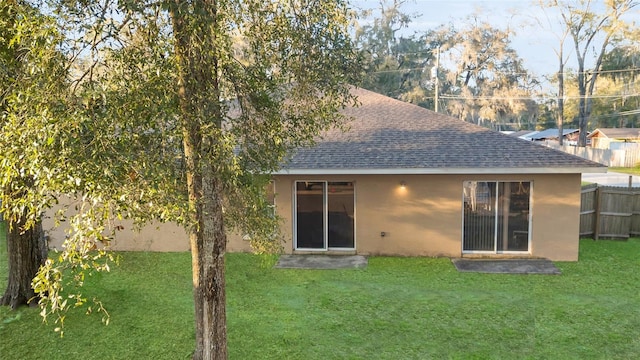 rear view of house featuring a yard, fence, stucco siding, and roof with shingles