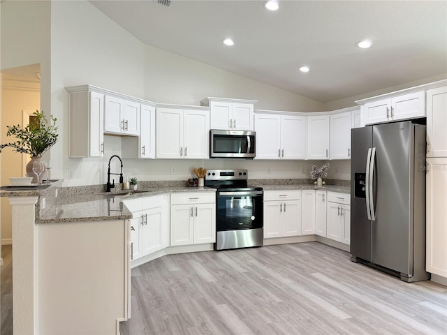 kitchen with light stone counters, stainless steel appliances, a peninsula, a sink, and white cabinets