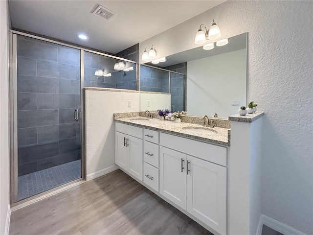 bathroom with wood finished floors, a sink, visible vents, and a shower stall