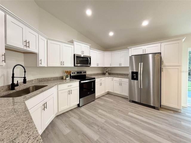 kitchen featuring light wood finished floors, white cabinets, light stone counters, stainless steel appliances, and a sink