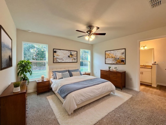 bedroom featuring baseboards, visible vents, a ceiling fan, light colored carpet, and ensuite bath