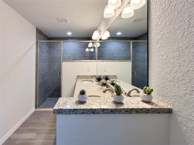 bathroom with visible vents, a sink, a shower stall, wood finished floors, and baseboards