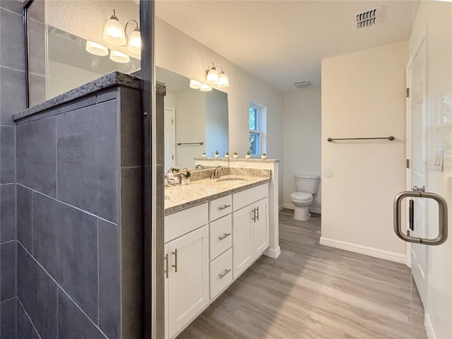 bathroom with wood finished floors, visible vents, toilet, vanity, and a walk in shower