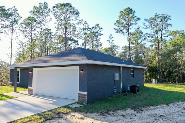 view of side of home featuring a yard, stucco siding, a shingled roof, central AC unit, and a garage