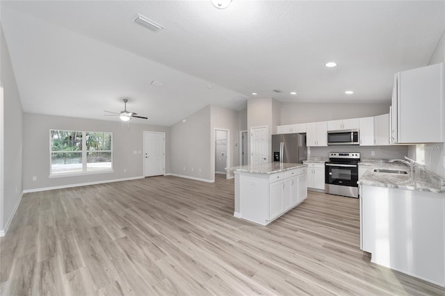 kitchen featuring stainless steel appliances, a sink, vaulted ceiling, light wood-type flooring, and a center island