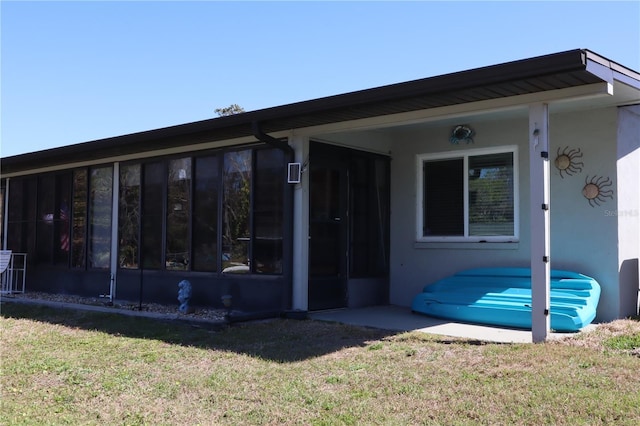 back of house with a yard, a sunroom, and stucco siding