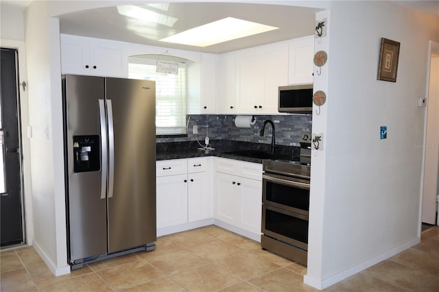 kitchen featuring baseboards, white cabinets, appliances with stainless steel finishes, backsplash, and a sink