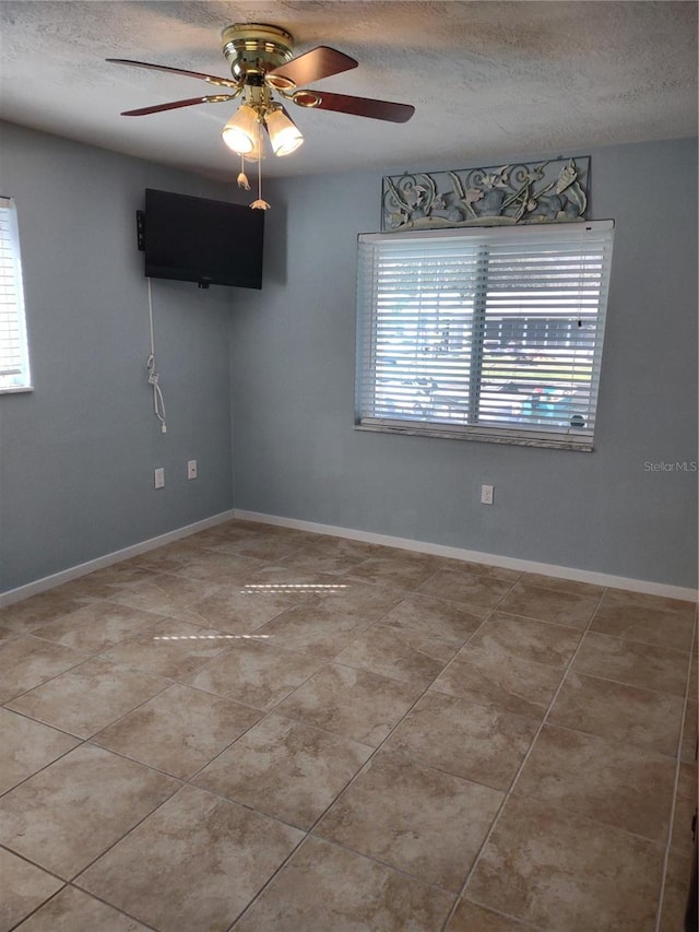 empty room with a textured ceiling, baseboards, and light tile patterned floors