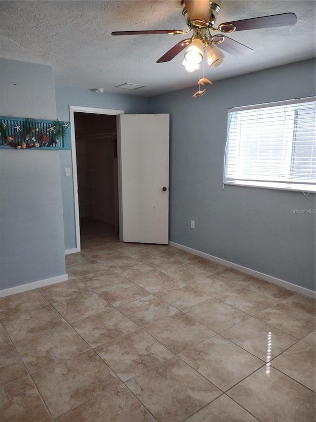 spare room featuring a textured ceiling, light tile patterned floors, and baseboards