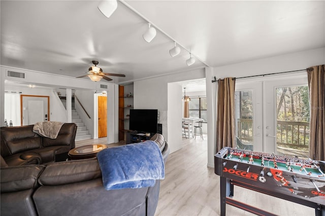 living room featuring a ceiling fan, visible vents, light wood-style flooring, and stairs