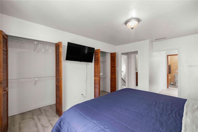 bedroom featuring light wood finished floors, visible vents, and two closets