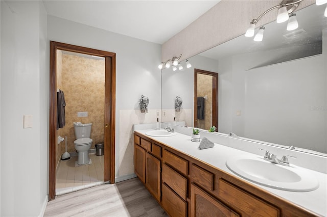 bathroom featuring double vanity, wood finished floors, a sink, and toilet