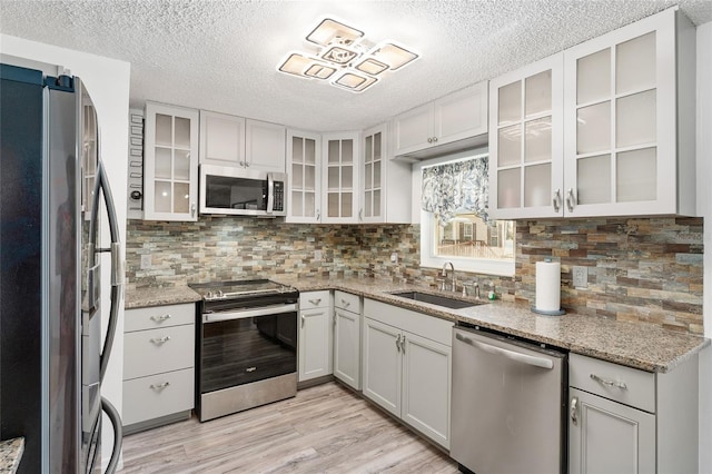 kitchen featuring a sink, light stone counters, backsplash, stainless steel appliances, and light wood-style floors