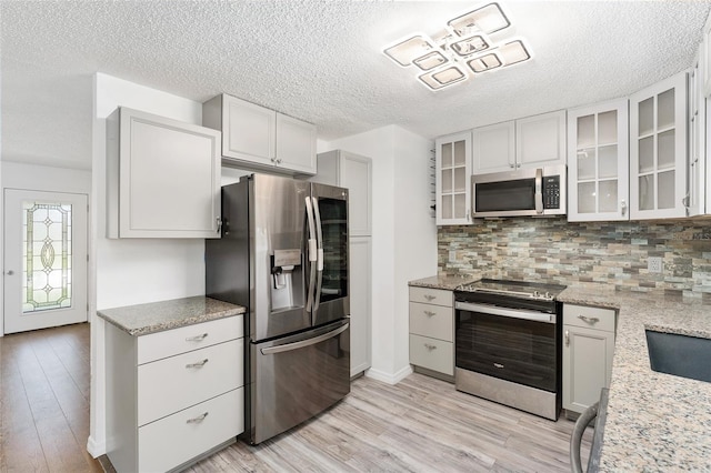 kitchen with decorative backsplash, glass insert cabinets, light wood-type flooring, and appliances with stainless steel finishes