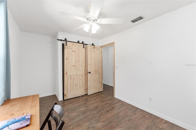 unfurnished office featuring a ceiling fan, wood finished floors, visible vents, baseboards, and a barn door