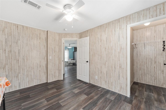 spare room with visible vents, wooden walls, wood finished floors, and a ceiling fan