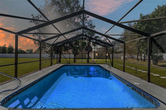 pool at dusk featuring fence, a lawn, glass enclosure, a patio area, and an outdoor pool