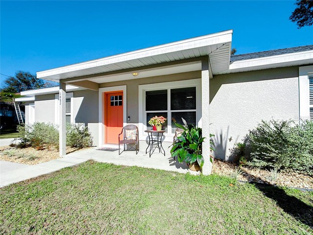 view of exterior entry with a porch, a lawn, and stucco siding