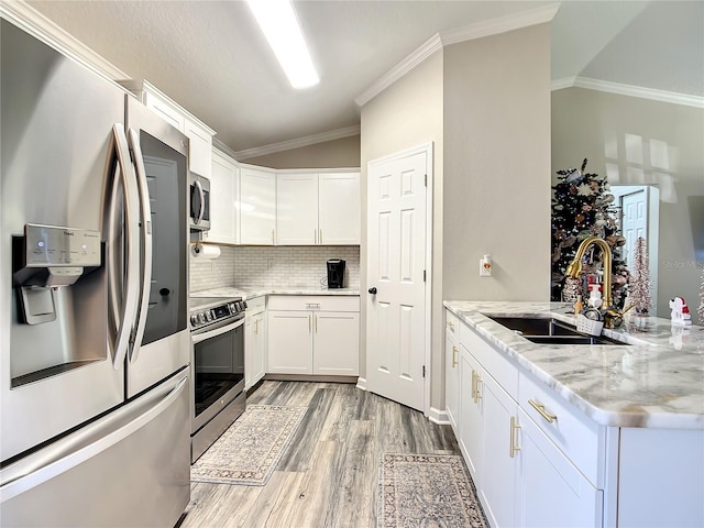 kitchen with light wood finished floors, appliances with stainless steel finishes, ornamental molding, a sink, and a peninsula