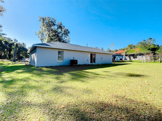 rear view of house featuring stucco siding, central AC unit, and a yard