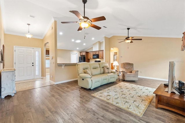 living room featuring arched walkways, wood finished floors, lofted ceiling, and ornamental molding