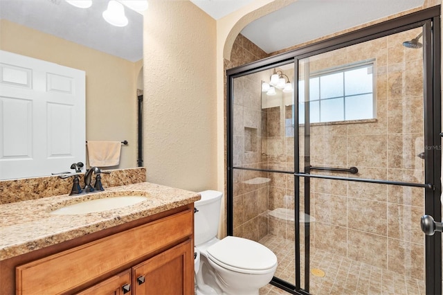 bathroom with toilet, a stall shower, a textured wall, and vanity