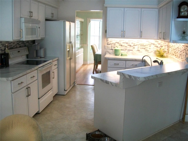 kitchen featuring white appliances, white cabinets, a peninsula, and backsplash