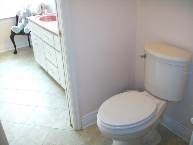 half bath with toilet, tile patterned floors, baseboards, and vanity