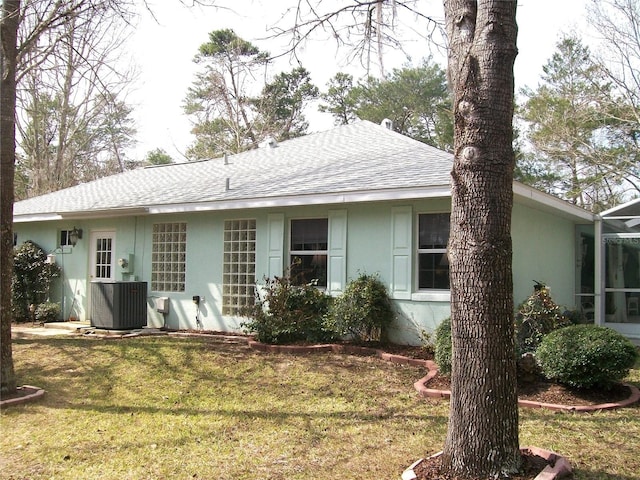 rear view of property with stucco siding, central AC unit, a lawn, and roof with shingles