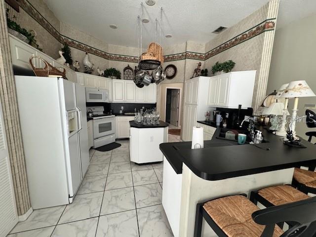 kitchen with dark countertops, a peninsula, marble finish floor, white appliances, and a sink