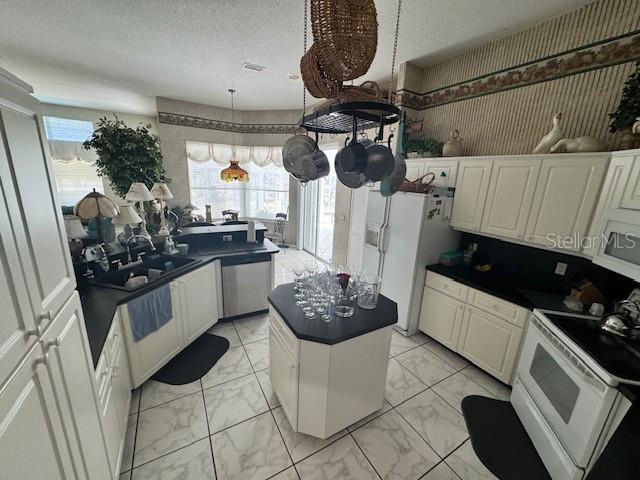 kitchen featuring white appliances, a sink, a textured ceiling, dark countertops, and marble finish floor