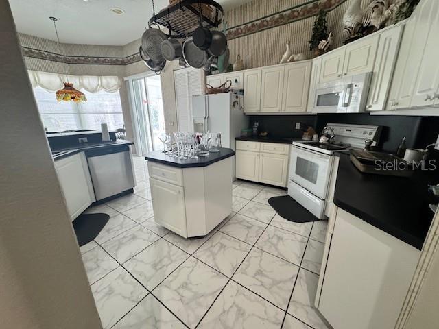 kitchen featuring marble finish floor, dark countertops, a kitchen island, white cabinetry, and white appliances